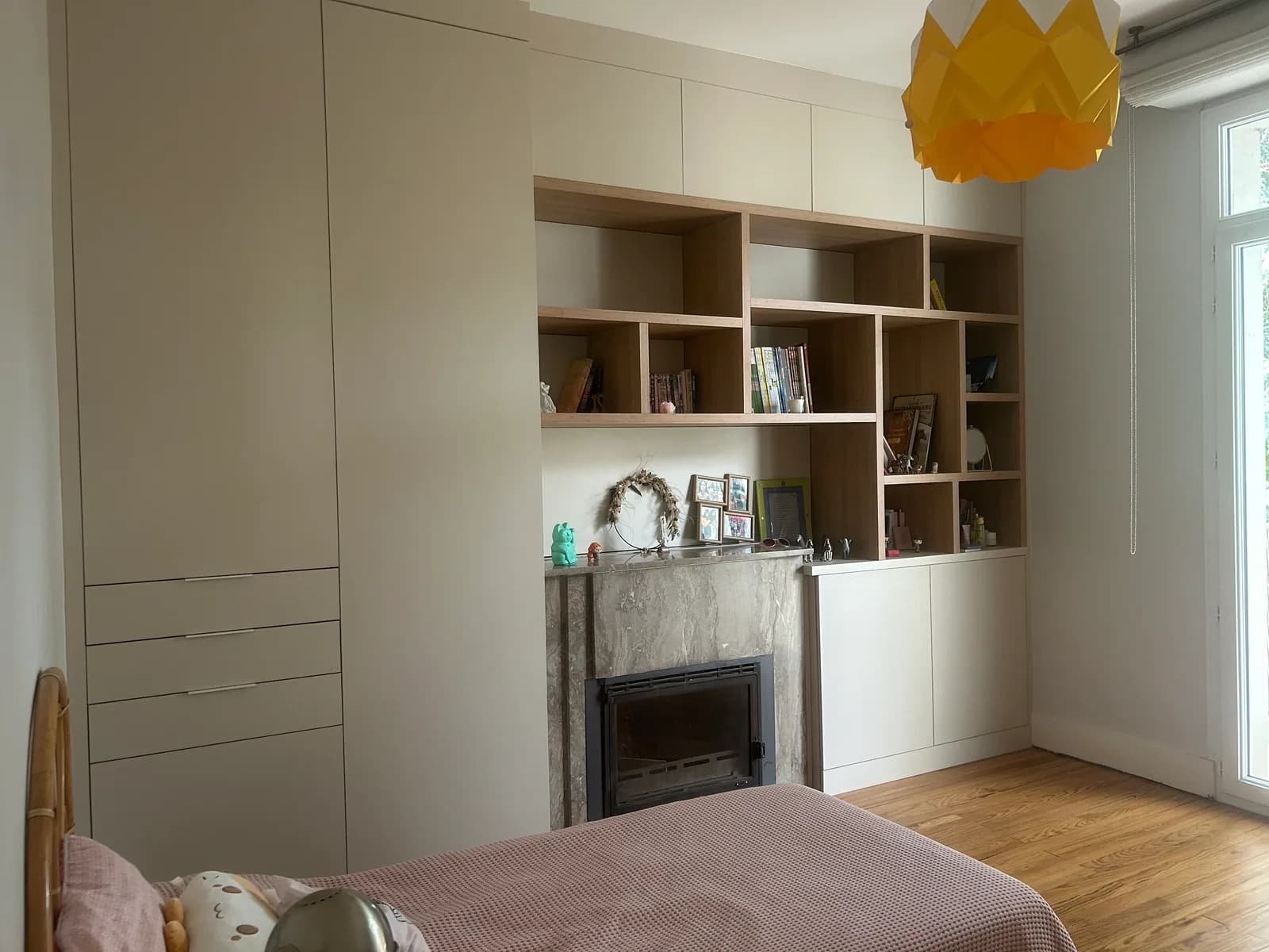 Bibliothèque beige avec niches en chêne encadrant une cheminée en marbre, colonnes de rangement et tiroirs.