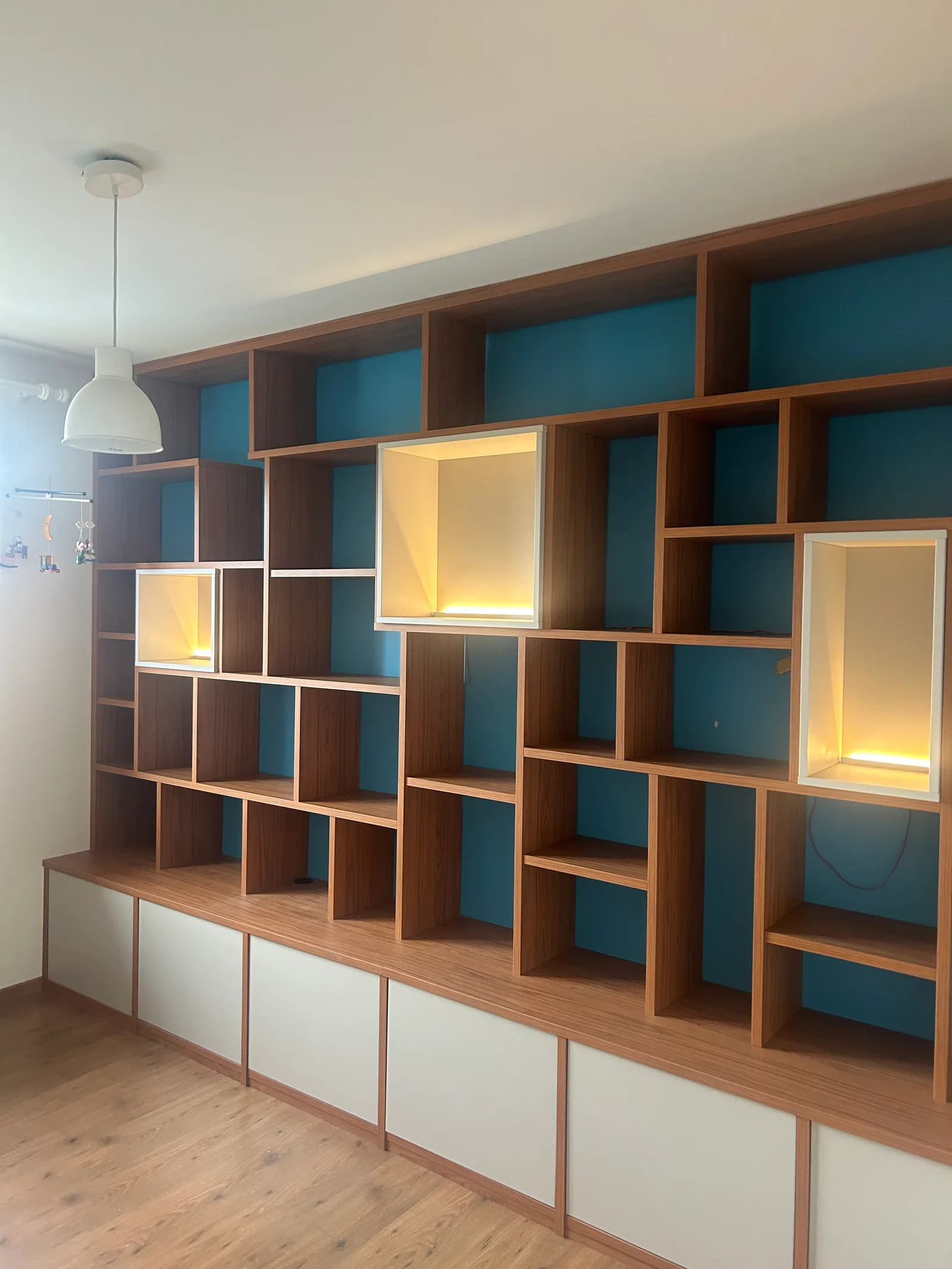 Bibliothèque toute largeur en noyer à fonds bleus, caissons blancs rétroéclairés et meuble bas à portes blanches.