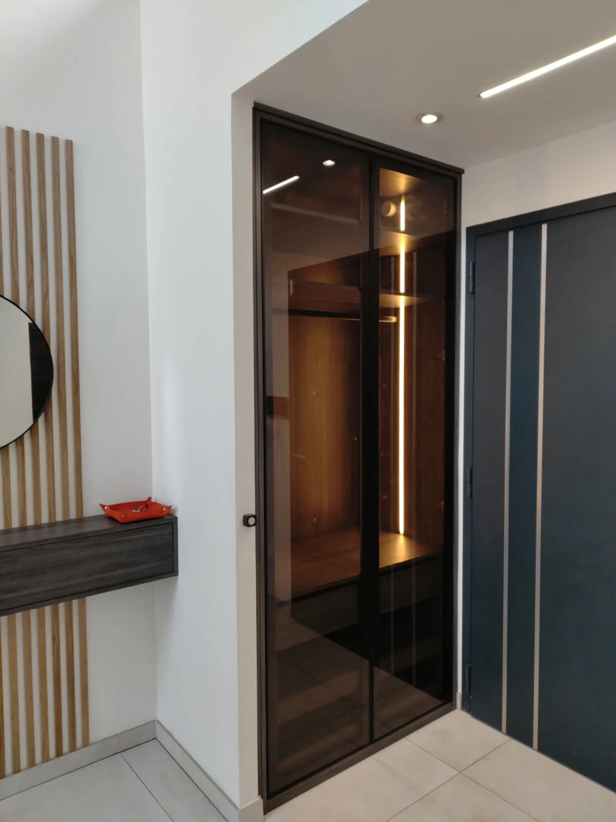 Dressing d'entrée fermé par des portes vitrées en verre fumé type verrière, intérieur bois éclairé par LED