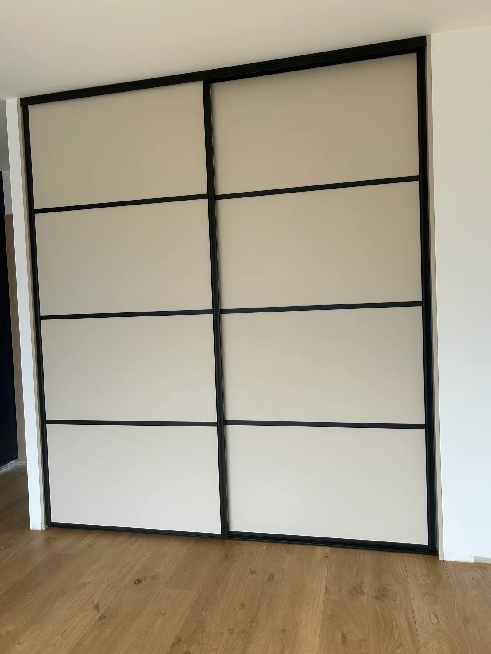 Grandes portes coulissantes laquées blanc cassé à croisillons noirs de style japonisant dans une chambre