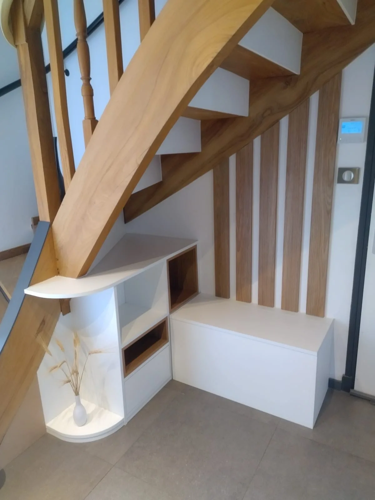 Aménagement sous escalier blanc et chêne avec banc-coffre, niches ouvertes et claustra à tasseaux